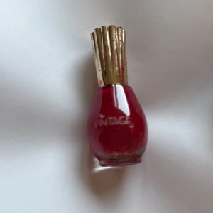Vintage rött nagellack med guldfärgat lock - Snyggt rött nagellack från Vintage med en elegant, rundad glasflaska och ett dekorativt guldfärgat lock. Perfekt för dig som vill ha en klassisk och djup röd färg på naglarna. Flaskan har en lyxig retrostil som sticker ut i sminkväskan.