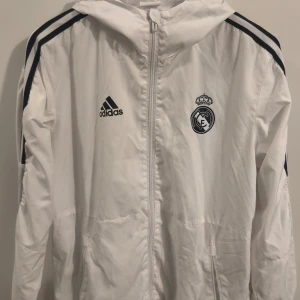 Real Madrid träningsjacka - En riktig snygg träningsjacka/vindjacka som är perfekt för träning utomhus, eller helt enkel en promenad ute. Har använts max 5-6 gånger.   Har du några frågor eller vill ha bilder, bara att fråga på!