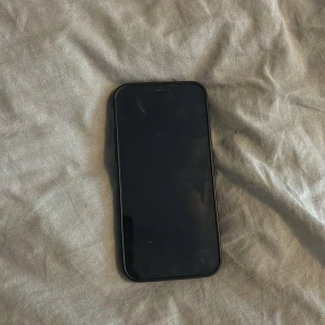 iPhone 12 - Snygg svart iPhone 12 med dubbla kameror. Telefonen har synliga repor och slitage på baksidan, men skärmen ser hel ut. Perfekt för dig som vill ha en kraftfull iPhone till ett bra pris. Säljs i befintligt skick.