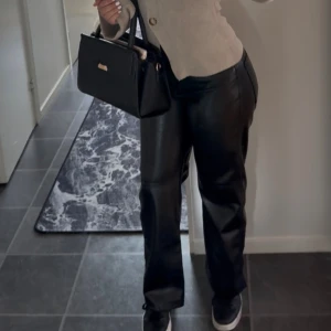Svarta vida byxor i skinnimitation - Säljer ett par svarta byxor i skinnimitation med rak och vid passform. Byxorna har medel midja och ger en cool, trendig look. Endast använda en gång 