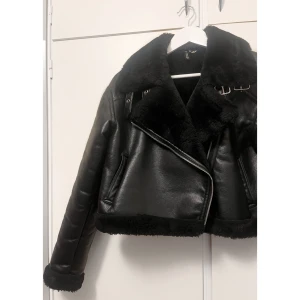 Svart teddy bikerjacka från H&M - Säljer en svart bikerinspirerad teddyjacka från H&M. Jackan är croppad och har dragkedja framtill samt mjukt material på insidan och vid ärmslut. Perfekt för kalla dagar!