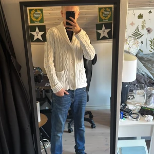 Vit kabelstickad kofta från GANT XS - Vit kabelstickad kofta från GANT i stretchig bomull. Koftan har sjalkrage, tre stora knappar framtill och två fickor. Snygg och klassisk modell som passar perfekt till jeans eller chinos.