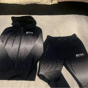 Svarta mjukisbyxor från BOSS - Snyggt svart mjukis sett från Hugo BOSS med vit pixelmönstrad design och logga. Setet har snörning i midjan och dragkedjefickor.