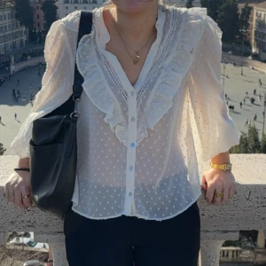 Vit volangskjorta med prickar Zara - Supersöt vit blus från Zara med volangdetaljer längs v-ringningen och knappar framtill. 