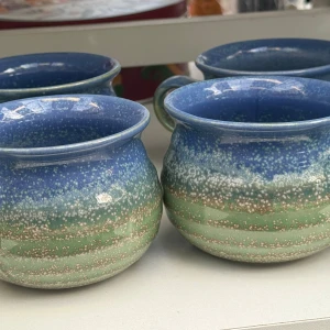 Fyra muggar - keramikmuggar med blå och gröna nyanser och prickigt mönster. Muggarna har en rundad form och en bred öppning, vissa med handtag. Ytan är blank och ser välbevarad ut utan synligt slitage eller sprickor. Perfekt för te eller kaffe och ger en unik känsla till hemmet.