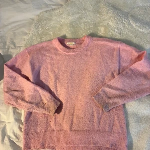 Rosa stickad tröja från Gina Tricot - Mysig rosa stickad tröja från Gina Tricot med rund halsringning och ribbade muddar. Perfekt för lager-på-lager och chill dagar. Enkel och stilren design som är lätt att matcha med jeans eller kjol.