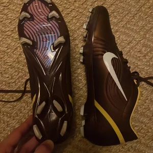 Nike fotbollsskor  - Nypris 3000-4000. Skorna är använda en gång och är i perfekt skick. Snygga fotbollsskor från Nike i svart med gula detaljer och vit swoosh. Skorna har snörning och mönstrad yttersula med dobbar för bra grepp på planen. Tillverkade i syntetmaterial med sportig design och smidig passform.