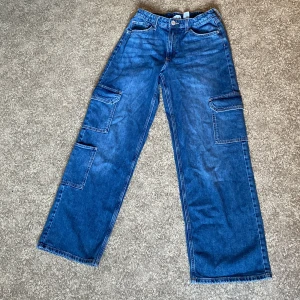 Blå wide leg cargopants från H&M - Säljer ett par blå cargopants från H&M med breda ben och låg midja. Byxorna har justerbar midja och stora fickor på sidorna. Har använts ett fåtal gånger, men har inga defekter. Kom gärna med prisförslag!