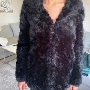 Svart pälsjacka med huva - Mysig svart pälsjacka med huva och lång ärm. Jackan har en fluffig och lyxig känsla, perfekt för kalla dagar. Stängs framtill med diskret knäppning och har en rak passform som ger en snygg siluett.mycket bra skick.använd 1 gång. Fräsch. Vi är rök-djurfri familj.