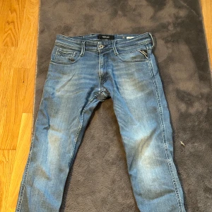 Replay blå jeans  - Säljer ett par snygga blå jeans från Replay med klassisk femficksdesign och raka ben. Jeansen har ljusa slitningar framtill och bak, samt detaljerade bakfickor med broderade mönster. Perfekt passform och stilren look för dig som gillar streetwear.