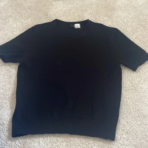 Svart kortärmad tröja från H&M XS - En stilren svart kortärmad tröja från H&M i storlek XS. Tröjan har rund halsringning och ribbade detaljer vid ärmslut och nederkant. Perfekt för en clean och enkel look, lätt att matcha med allt. Pris kan diskuteras 