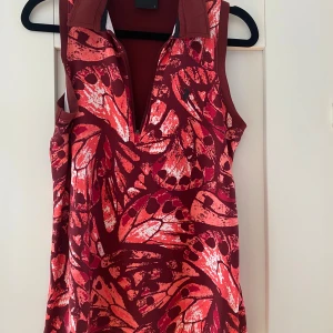 Röd mönstrad tränningslinne Peak Performance - Säljer en cool träningslinne från Peak Performance i rött med ett abstrakt mönster i olika röda och rosa nyanser. Linnet är ärmlös, har krage och dragkedja framtill. Materialet är mjukt och stretchigt, perfekt för dig som gillar sportig stil. Mått Över bröstet: ca 43 cm Längd från axeln och ner: ca 64 cm  88% polyester och 12% elastan  Kommer från ett djur och rökfritt hem