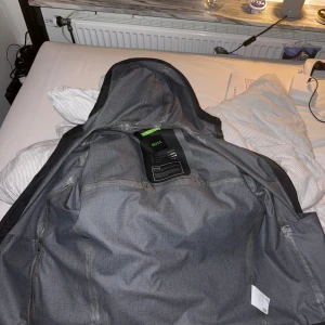Svart vindjacka från BOSS med huva - Säljer en svart vindjacka från BOSS med huva och diskret logga på ärmen. Jackan är lätt, vattenavvisande och har tekniskt laminerat tyg med tejpade sömmar. Perfekt för dig som vill ha en stilren och funktionell jacka med snygg passform. Nypris 4300, kan gå ner i pris bara att skicka prisförslag så tar vi det därifrån🙏