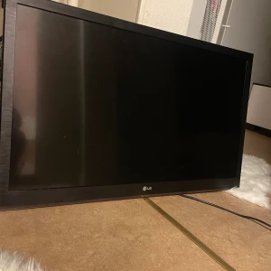 LG TV 42tum - LG platt-TV med svart ram, klassisk design. Skärmen ser hel ut utan synliga sprickor eller större repor. Perfekt för vardagsrummet eller som extra TV. Strömkabel synlig, men fjärrkontroll och stativ ingår ej på bilden. Fint skick.