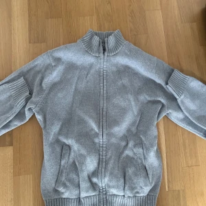 Grå kofta med dragkedja från L.L. Bean - Säljer en grå kofta från L.L. Bean i 100% bomull. Tröjan har ribbad krage, muddar och nederkant samt hel dragkedja framtill. Perfekt för lager-på-lager och chill dagar. Två fickor framtill och klassisk passform.