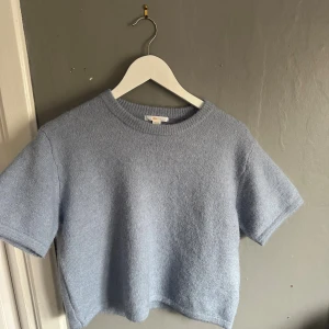 Ljusblå stickad tröja Gina Tricot - Superfin ljusblå stickad tröja från Gina Tricot med kort ärm och rund halsringning. Tröjan är croppad och har en mjuk, mysig känsla som passar perfekt till jeans eller kostymbyxor. Enkel och stilren design som är lätt att matcha.