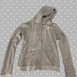 Grå hoodie från Abercrombie & Fitch - Grå hoodie från Abercrombie & Fitch i storlek L. Klassisk modell med dragkedja framtill, huva med snörning och två fickor. Mjuk och skön, perfekt för chill dagar. Diskret logga på bröstet. Enkel och stilren design som funkar året runt.