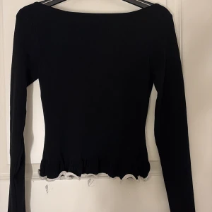 Svart stickad tröja med volangkant - Supersöt svart stickad tröja med långa ärmar och volangkant i vitt längs nederkanten och ärmsluten. Tröjan har en smickrande passform och känns både trendig och stilren. Perfekt att styla med jeans eller kjol för en snygg look. Ordinarie pirs 400❣️hoppas den kan komma till användning hos nån annan!✨