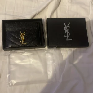 Svart YSL plånbok i skinn - Supersnygg svart plånbok från YSL med guldigt logodetalj framtill. Pris kan diskuteras vid snabb affär!