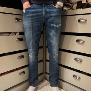 Dondup George med slitningar - Snygga blå jeans från Dondup med coola slitningar och en snygg tvättning. Jeansen har medelblå färgton och är tillverkade i mjukt denimtyg. Perfekta för en avslappnad och trendig look. Dom är i modellen George.                                                                         Skick=helt nya med tags nypris=3000