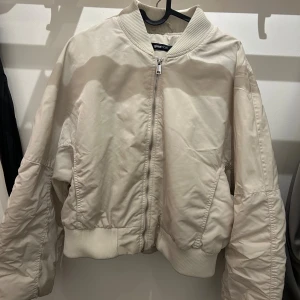 Beige bomberjacka från Gina Tricot - Snygg beige bomberjacka från Gina Tricot med ribbade muddar och krage. Jackan har dragkedja framtill, två sidofickor och är quiltad på insidan. Perfekt för dig som gillar en clean och enkel stil med lite oversized passform.