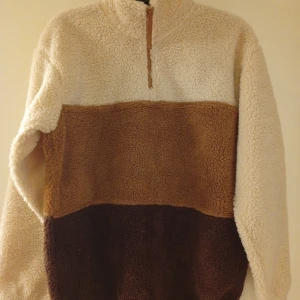 Färgglad fleece-tröja från Vailent - Mysig fleece-tröja från Vailent i storlek S. Tröjan har blockfärger i beige, ljusbrun och mörkbrun, samt en half zip-dragkedja framtill. Perfekt för kyliga dagar och har en riktigt skön oversized känsla.