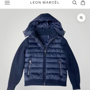 Marinblå pufferjacka från Leon Marcel - Snygg marinblå pufferjacka från Leon Marcel med stickade ärmar och quiltad front. Jackan har avtagbar huva, två dragkedjefickor och ribbade muddar. Jackan är helt ny, säljes pga felköp. Den finns inte kvar att köpa något stands