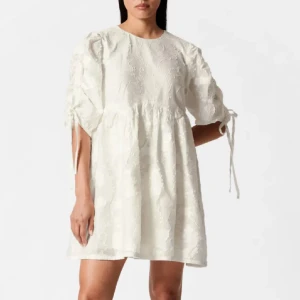 Vit broderad kortklänning med knytärmar från other stories - Supersöt vit kortklänning från other stories med broderade detaljer och voluminösa ärmar med knytband. Klänningen har en lös passform och rund halsringning. Perfekt för sommarens alla tillfällen!