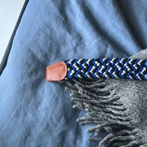 Blå och vit flätad bälte med skinn - Säljer ett snyggt flätat bälte med blå, vit och grå färg i ett randigt mönster. mycket bra skick