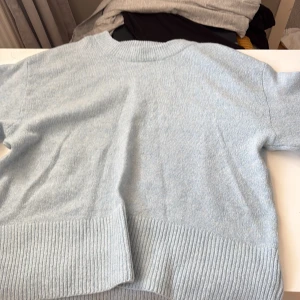 Ljusblå stickad tröja från Gina Tricot - Supermjuk ljusblå stickad tröja från Gina Tricot med bred ribbad kant nertill och vid ärmslut. Perfekt för lager-på-lager och chill dagar. Klassisk rund halsringning och relaxed fit.