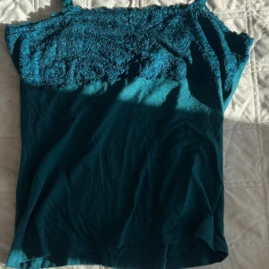 Turkos linnetopp med spets från Flash - Snygg turkos linnetopp från Flash med smala axelband och vacker spets upptill. Toppen har en enkel, rak passform och är perfekt för varma dagar. Materialet är mjukt och bekvämt, och spetsen ger en extra touch till looken.