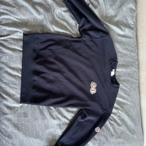 Mörkblå sweatshirt från Moncler - Snygg mörkblå sweatshirt från Moncler med broderad logga på bröstet och ärmen. Tröjan har rund hals, långa ärmar och ribbade muddar. Perfekt för dig som gillar stilrena märkesplagg med diskreta detaljer.