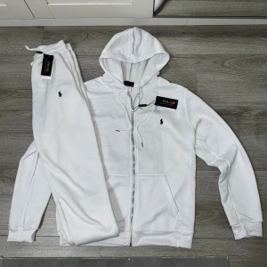Vit Tracksuit från Polo Ralph Lauren - Säljer en fräsch vit hoodie från Polo Ralph Lauren med dragkedja och huva. Tröjan har snörning vid huvan, två fickor fram och den klassiska broderade loggan på bröstet. Perfekt för chill dagar och snygg streetstyle. Ett till ett kvalité 