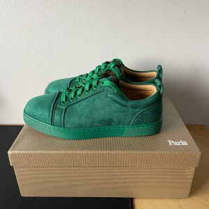 Gröna sneakers från Christian Louboutin - Snygga gröna sneakers från Christian Louboutin i mocka med klassisk röd sula och gröna snören. Insidan är i beige skinn och skon har en rund tå. Kommer med originalkartong och dustbag. Perfekt för dig som vill sticka ut med exklusiva detaljer.