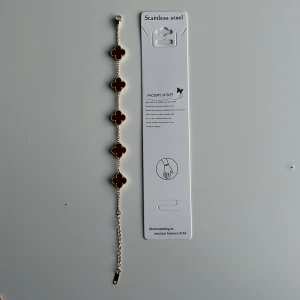 🍷 Wine/red-gold Alhambra bracelet  - Snyggt armband i guldtonad metall med fem röda fyrklöverformade länkar. Kan justeras i längd med kedja och har detaljerade kanter runt varje klöver. Perfekt för dig som gillar unika och färgstarka accessoarer. Mvh clover.se