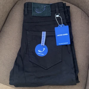 Svarta jeans från Jacob Cohen 30 - Svarta jeans från Jacob Cohen med klassisk femficksdesign och snyggt broderad logotyp på bakfickan. Byxorna har raka ben och är tillverkade i ett mjukt bomullsmaterial med en exklusiv känsla. Perfekt för dig som gillar stilrena och tidlösa plagg.