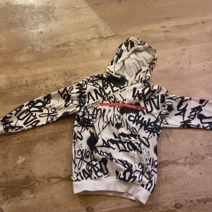 Vit och svart hoodie med graffiti från WOXO - Säljer en fett snygg hoodie från WOXO 720° i storlek 146/152. Den är vit med svart graffiti-inspirerat tryck över hela tröjan och har en huva. Materialet är mjukt och känns som bomull. Perfekt för dig som gillar streetstyle och vill sticka ut.