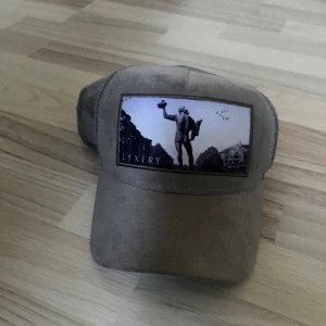 Grå keps från Lyxery med mesh - Säljer en grå keps från Lyxery by Sweden med mesh på sidorna och baksidan. Framsidan har en svartvit patch med motiv av en staty och stadsmiljö. Insidan är dekorerad med stadskarta och märkets logga. Perfekt för dig som gillar streetstyle och unika detaljer.