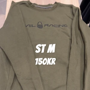Olivgrön Sail Racing sweatshirt M - Olivgrön sweatshirt från Sail Racing med tryckt logga över bröstet. Tröjan har rund halsringning, långa ärmar och ribbade muddar vid ärmslut och nederkant. Perfekt för en avslappnad och sportig stil.