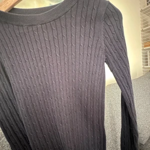 Svart kabelstickad tröja Gina Tricot - Kabelstickad svart tröja från Gina Tricot med rund halsringning och långa ärmar. Tröjan har ett klassiskt kabelmönster och är i mjukt stickat material, storlek S