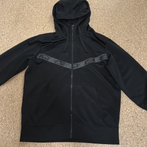 Svart träningsjacka med huva från Nike - Svart träningsjacka med huva och dragkedja framtill. Bekväm passform och mjukt material – perfekt till vardag eller gymmet. Använd ett fåtal gånger, i mycket bra skick. Inga fläckar eller hål