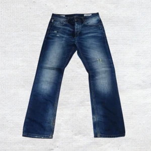 Vintage Jack & Jones distressed Archive bootcut wide loose washed blue Y2K jeans rare grisch - Riktigt häftiga blå jeans från Jack & Jones med slitna detaljer, snygg tvätt och klassisk femficksdesign. Jeansen har rak passform och normal midja, tillverkade i tåligt denim med coola slitningar framtill. Perfekta för en avslappnad streetstil.  Mått:  Längd - 105cm  Midja - 40cm  Benöppning - 20cm