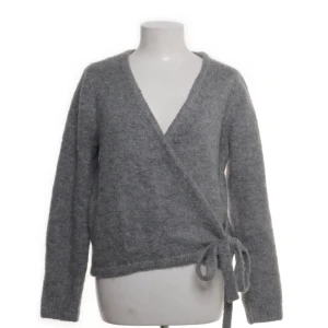 Grå omlott kofta från Designbyamor - Mysig grå stickad kofta från Designbyamor i omlottmodell med knyt i sidan. Tröjan har lång ärm och djup v-ringning. Materialet är mjukt och fluffigt och tröjan är väldigt varm så perfekt inför vintern. Den är i storlek S men den är stor i storleken så skulle säga att den passar M. Original pris 569kr. 