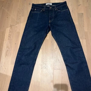 Mörkblå jeans från Jack & Jones - Snygga mörkblå jeans från Jack & Jones med klassisk femficksdesign och raka ben. Jeansen har kontrastsömmar och läderpatch bak i midjan. Perfekta för dig som gillar en enkel och stilren look.