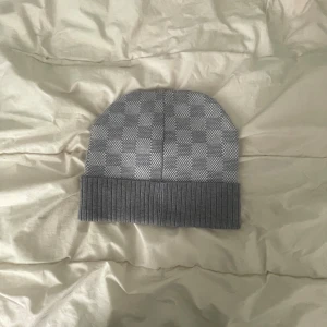 Grå mössa - Snygg grå mössa med rutigt mönster och bred, ribbad uppvikt kant. Perfekt accessoar för kyliga dagar och passar till de flesta outfits. Mjuk och bekväm passform.