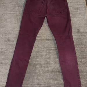 Vinröda skinny jeans - Säljer ett par vinröda jeans med skinny fit och klassiska fem fickor. Jeansen har en snygg sliten detalj vid knät och är tillverkade i mjukt bomullsmaterial med lite stretch. Perfekt för dig som gillar en smal siluett och vill sticka ut med färg.