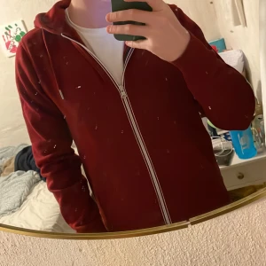 Vinröd hoodie från Tommy Hilfiger - Vinröd hoodie från Tommy Hilfiger med dragkedja och huva. Klassisk logga på bröstet och vita detaljer på dragkedjan. Mjuk insida och långärmad modell, perfekt för höst och vinter. Snygg och enkel att matcha med jeans eller joggers. Ny pris över 1000 lappen, så bättre skick o pris finns inte!