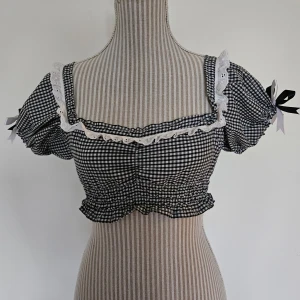 Svart och vit rutig handmade topp från Emma Jane Clothing  - Handsydd rutig topp från Emma Jane Clothing med puffärmar och ginghammönster. Endast använt den ett fåtal gånger, mycket fint skick. ''Onesize'' men uppskattar att den passar XXS-S. Jag köpte den för ca 1050 kr med frakt och importmoms inräknat.  Rökfritt hem men har katter.