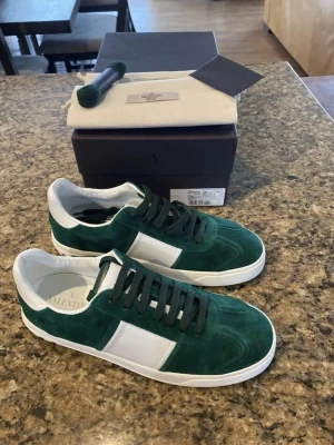 Valentino flycrew topp skick - Säljer ett par Valentino Garavani Rockstud sneakers i mörkgrönt och vitt. Skorna har snygga nitar på sulan, snörning och är tillverkade i mocka och skinn. Klassisk rund tå och platt sula. Kommer med originalkartong och extra skosnören. Ej använda , nytt skick.