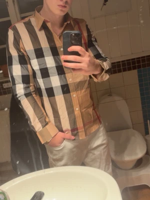 Burberry rutig skjorta i bomull - Säljer en klassisk Burberry skjorta med stort rutmönster i beige, svart, vit och röd. Skjortan har lång ärm, knappar framtill och är tillverkad i mjuk bomull. Perfekt för dig som gillar ikoniska designer och vill sticka ut med en snygg look. Storlek XL men skulle säga den sitter mer som L